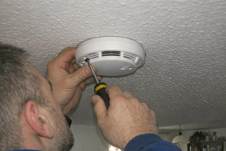 Installateur befestigt einen Rauchmelder an einer frisch gestrichenen Schlafzimmerdecke